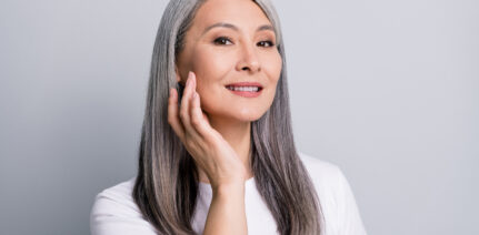 Photo portrait of senior woman with grey hair touching cheek wearing white t-shirt smiling isolated on grey color background.