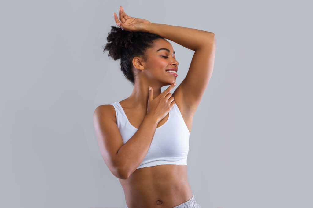 Happy black girl smelling her fresh armpit over grey background, putting hand up, copy space