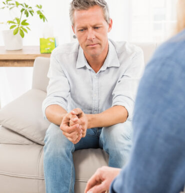 Worried man sitting on couch and talking to therapist in the office